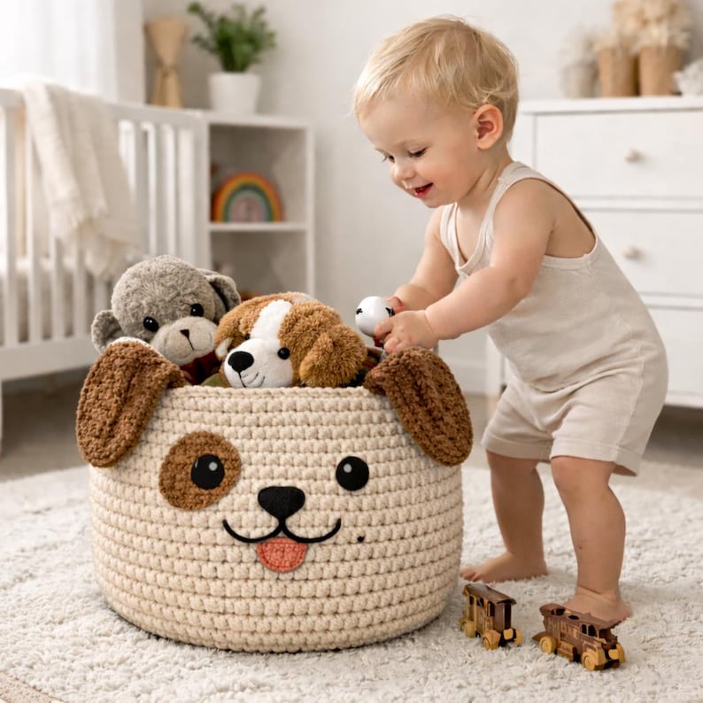May include: A cream-colored, crocheted dog-faced storage basket filled with plush toys. The basket has brown ears, eyes, and a pink tongue. A child is playing with the toys. Two wooden toy trains are on the floor.