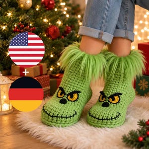 Op de afbeelding: Een paar felgroene gehaakte pantoffels met een pluizige rand van imitatiebont aan de bovenkant. De pantoffels zijn versierd met geborduurde gele ogen met zwarte pupillen en een gestikte zwarte mond, wat een karakteristiek gezicht vormt.