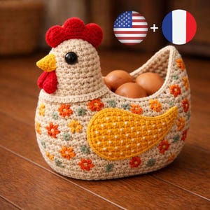 Puede incluir: Una cesta de huevos hecha a mano con forma de gallina de ganchillo. La cesta es de color beige con motivos florales naranjas, amarillos y verdes. Tiene una cresta y una barbilla rojas, un pico amarillo y un ojo negro. La cesta contiene huevos marrones.