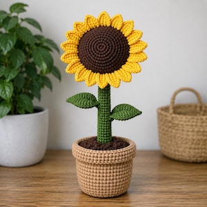 Puede incluir: Un girasol de ganchillo en una maceta de color tostado. La flor tiene un centro marrón oscuro, pétalos amarillos brillantes y un tallo verde con dos hojas. La maceta está rellena de tierra de ganchillo marrón oscuro. Todo está hecho de hilo.