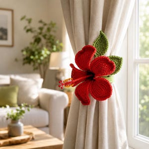 May include: A crochet curtain tieback featuring a large, vibrant red hibiscus flower with five rounded petals and a prominent stamen tipped with yellow pollen, accented by two textured green leaves attached to a matching green circular band.