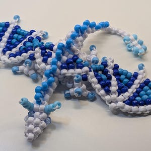 May include: A beaded dragon figurine in white, light blue, and dark blue. The dragon has outstretched wings and a long tail. The wings and body are made of small, round beads.