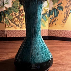 Peut inclure: Un vase élégant et élancé avec un bord évasé et festonné. Le vase présente une finition brillante avec un dégradé de couleurs, passant d'une base noire profonde à un corps tacheté de vert et de bleu sarcelle. Le vase est probablement en céramique ou en verre.