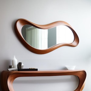 Puede incluir: Un moderno juego de consola y espejo de madera. El espejo tiene una forma orgánica única. La consola tiene un diseño curvo con un centro abierto. El conjunto está hecho de madera de tonos cálidos y se muestra contra una pared neutra.