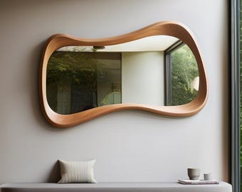 May include: A contemporary wooden mirror with an unusual, flowing shape is mounted above a bench with a grey cushion. The bench has a curved design and a lower shelf. A small cushion and two cups are on the bench. The room has a minimalist design.