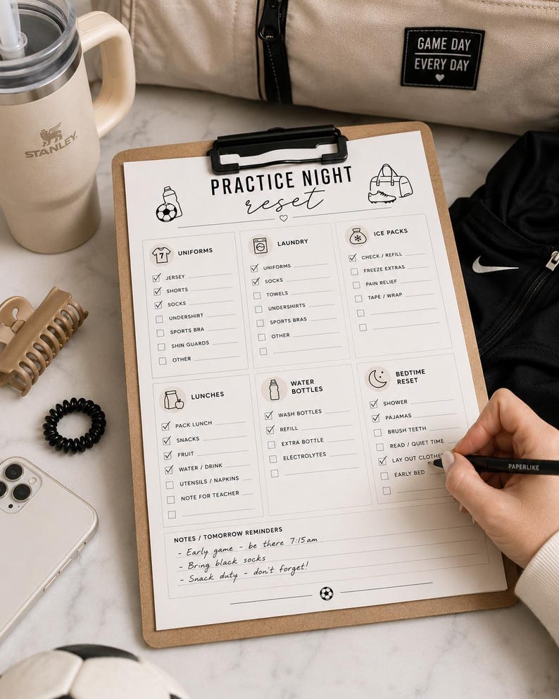 May include: A clipboard with a checklist titled "Practice Night Reset" is being filled out with a pen. The checklist includes sections for uniforms, laundry, ice packs, lunches, water bottles, and bedtime reset. A Stanley tumbler and a beige bag are in the background.