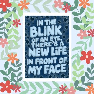 May include: A digital art print with a light blue background and a white frame. The text "IN THE BLINK OF AN EYE, THERE'S A NEW LIFE IN FRONT OF MY FACE" is in the center. The print is decorated with flowers and leaves.