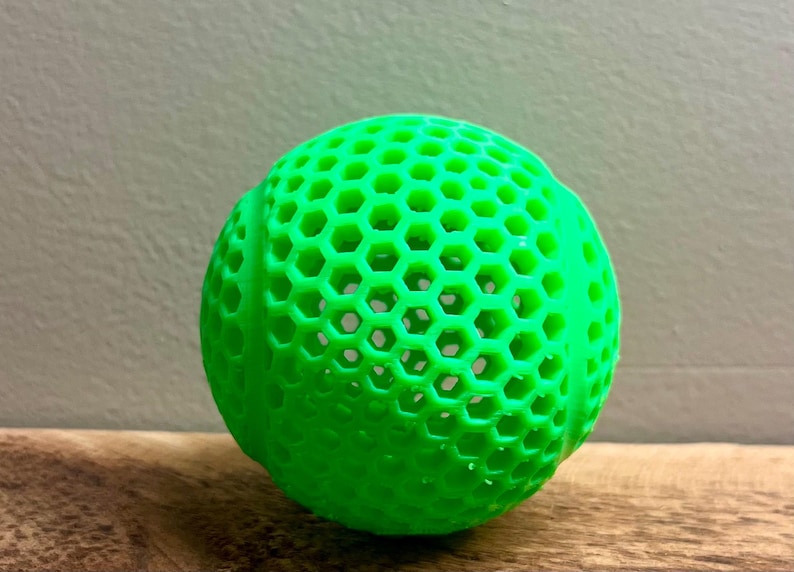 May include: A bright green, spherical object with a honeycomb pattern. The ball is made of a solid material and has a textured surface. The object is sitting on a wooden surface.
