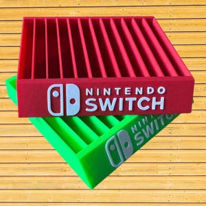 May include: Red and green Nintendo Switch game cartridge holders. The red holder is on top, with the Nintendo Switch logo and text in white. The green holder is underneath, also with the Nintendo Switch logo and text in white.