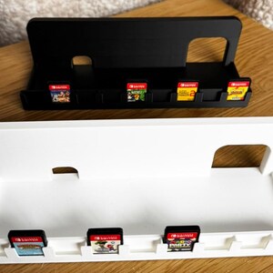 May include: Black and white game cartridge holders. The black holder has four game cartridges, and the white holder has three. The holders are designed to hold Nintendo Switch game cartridges. The holders are made of plastic.