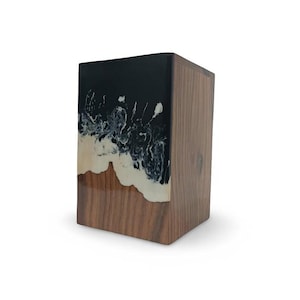 May include: A rectangular wooden block with a unique design. The top is black with white swirls, resembling a stormy sea. The middle section is a creamy color, and the bottom is a natural wood grain.