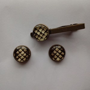 May include: A set of accessories featuring a reptile scale pattern. The set includes a tie clip and two matching round cufflinks. The metal has a bronze finish, and the scale pattern is in shades of brown and cream.