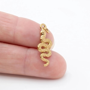 Peut inclure: Un charm en forme de serpent doré avec une surface texturée. Le charm est enroulé, avec une boucle en haut pour l'attacher à un collier ou un bracelet. Le charm mesure environ 3,8 cm de long.