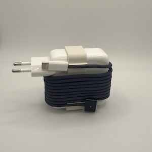 Puede incluir: Un adaptador de corriente blanco con un puerto USB-C y un enchufe de dos clavijas. El cable azul oscuro está enrollado alrededor del adaptador y asegurado con una correa blanca. El cable mide aproximadamente 120 cm.