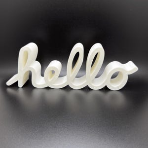 Könnte beinhalten: Ein cremefarbenes "Hallo"-Schild in Schreibschrift. Das Wort besteht aus einem festen Material und wird auf einem dunklen Hintergrund angezeigt. Die Buchstaben sind verbunden und haben ein abgerundetes, fließendes Design, geeignet für die Inneneinrichtung.