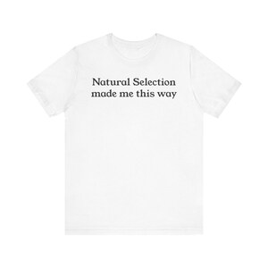 May include: White t-shirt with the text "Natural Selection made me this way" in a black, sans-serif font. The shirt is a crew neck style and appears to be made of a soft material.