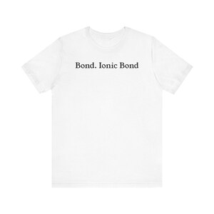 May include: White t-shirt with the text "Bond. Ionic Bond" printed in black. The shirt is made of a soft material and has short sleeves and a crew neck. The text is centered on the chest.