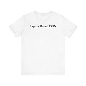 May include: White t-shirt featuring the black text "I speak fluent JSON" across the chest. The shirt has a crew neck and short sleeves. The material looks soft and lightweight, suitable for casual wear.