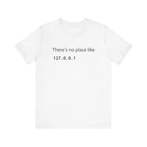 May include: White t-shirt with the text "There's no place like 127.0.0.1" printed in black. The shirt is a short-sleeved crew neck style.
