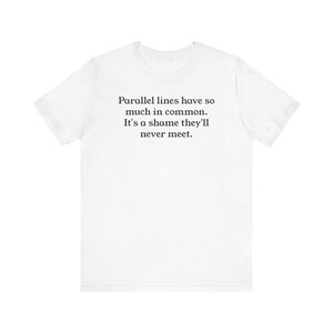 Peut inclure: T-shirt blanc avec l'inscription noire : "Les lignes parallèles ont tellement en commun. C'est dommage qu'elles ne se rencontrent jamais." Le t-shirt a des manches courtes et un col rond.