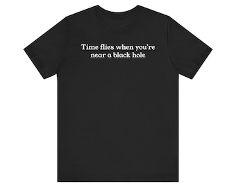 May include: Black t-shirt with the white text "Time flies when you're near a black hole." The shirt has short sleeves and a crew neck. The text is centered on the front of the shirt.
