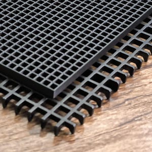 Puede incluir: Dos rejillas de plástico negro apiladas sobre una superficie de madera. Las rejillas tienen un patrón de cuadrícula cuadrada. La rejilla superior es rectangular y la inferior tiene un diseño de borde ligeramente diferente. Las rejillas son de plástico duradero.