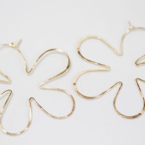 May include: A pair of gold flower-shaped hoop earrings. The earrings are made of thin, hammered metal and have a delicate, feminine look.