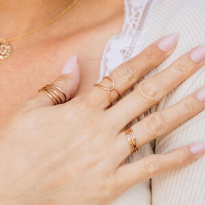 A close-up of a person's hand wearing multiple rings, including a ring with a unique design and another ring with a simple band.