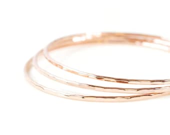 May include: Three thin, hammered gold rings stacked together. The rings are smooth and shiny, and they have a delicate, feminine look.