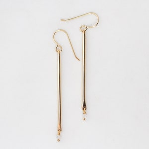 Image features our 14 karat yellow gold filled delicate and lightly hammered birthstone pendulum earrings. Featuring Herkimer diamonds, as the birthstone drop, these minimal earrings are the perfect gift for her and great for every day wear.