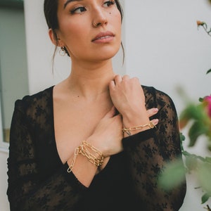 Puede incluir: Una mujer con un top de encaje negro con pulseras de cadena dorada en la mu&ntilde;eca.