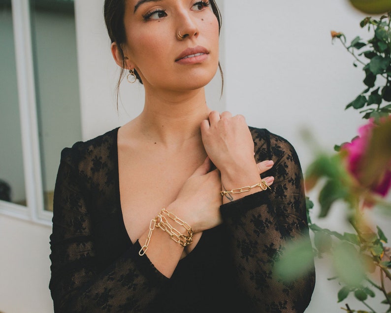 Puede incluir: Una mujer con un top de encaje negro con pulseras de cadena dorada en la mu&ntilde;eca.