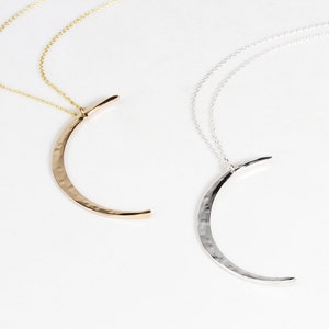 Image shows close up of both our sterling silver and 14 karat yellow gold filled moons. Delicately and intentional hand hammered to mimic the look of the moon, these handcrafted moons are made by our team of local artists. Moon measures 44mm long.
