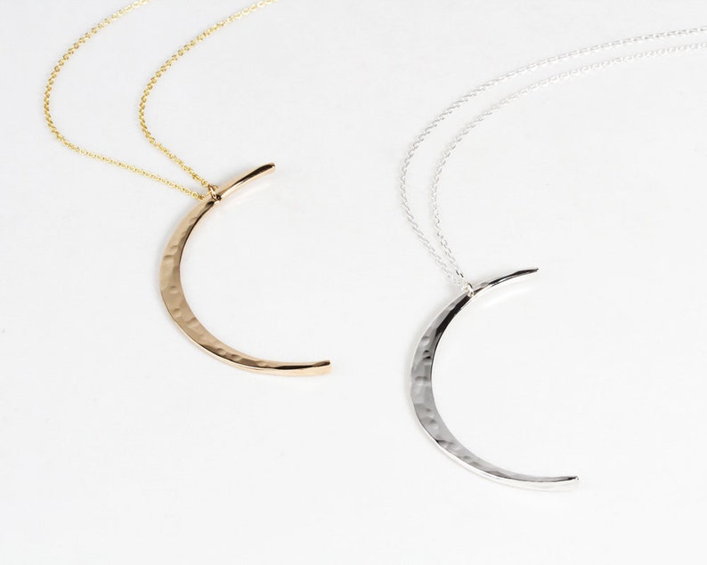 Image shows close up of both our sterling silver and 14 karat yellow gold filled moons. Delicately and intentional hand hammered to mimic the look of the moon, these handcrafted moons are made by our team of local artists. Moon measures 44mm long.