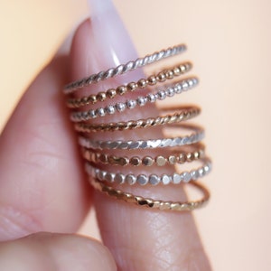 Textured stacking rings in 14 karat yellow gold filled and sterling silver shown holding between fingers. Stackable and high quality, meant to stack up and mix and match.