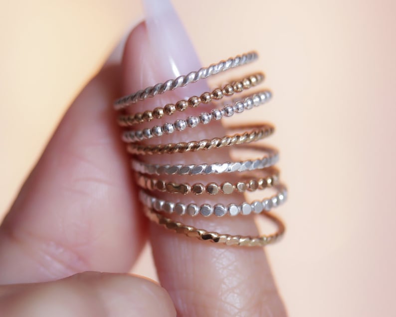 Textured stacking rings in 14 karat yellow gold filled and sterling silver shown holding between fingers. Stackable and high quality, meant to stack up and mix and match.