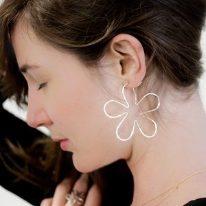 May include: Silver flower-shaped hoop earrings. The earrings are large and have a delicate, hammered texture.