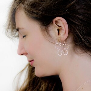 May include: A woman wearing silver flower-shaped earrings. The earrings are dangling and have a delicate, openwork design.