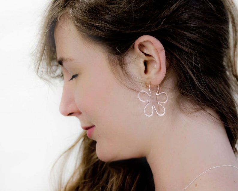 May include: A woman wearing silver flower-shaped earrings. The earrings are dangling and have a delicate, openwork design.