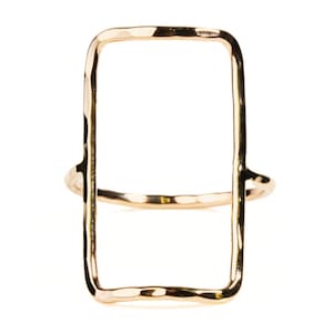 May include: A gold-colored ring with a rectangular open design. The ring has a hammered texture and a simple band. The rectangular shape is the focal point of the ring, creating a modern and minimalist aesthetic.