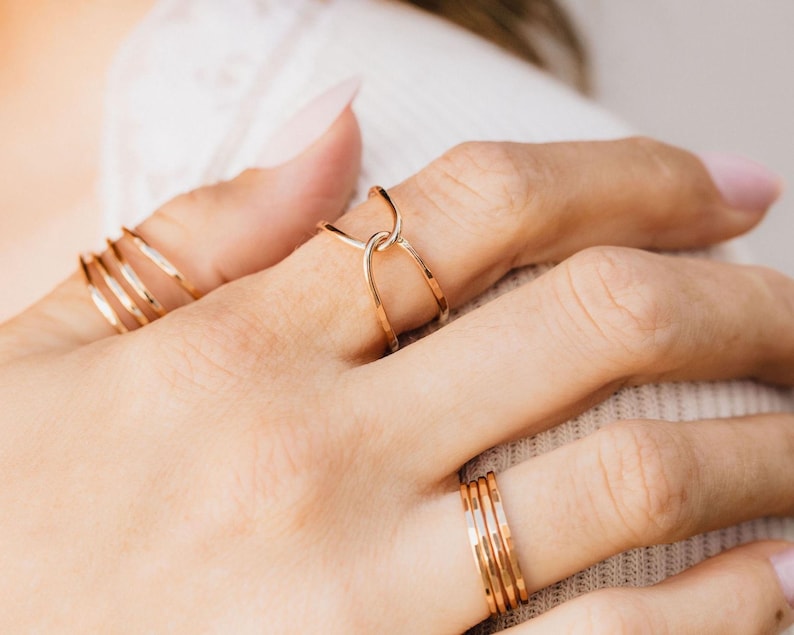 A close-up view of a person's hand wearing multiple gold rings on different fingers.