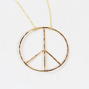 Image shows close up of our Inner Peace Necklace in 14 karat yellow gold filled. This powerful peace sign necklace tells a story as you wear it. Handcrafted from start to finish, this chic statement necklace is offered in sterling silver or gold fill