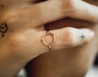 Può includere: Un anello d'oro con una finitura martellata e un design circolare. L'anello è indossato su un dito.