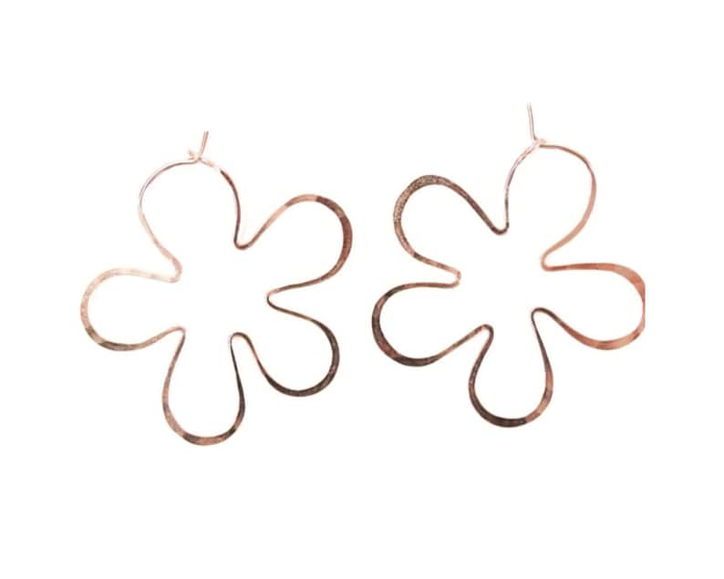 May include: A pair of rose gold flower-shaped hoop earrings. The earrings are made of thin metal and have a delicate, feminine look.
