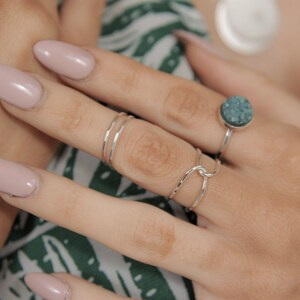 A close-up of a person's hand wearing multiple rings, including a ring with a blue stone and another ring with a twisted design.
