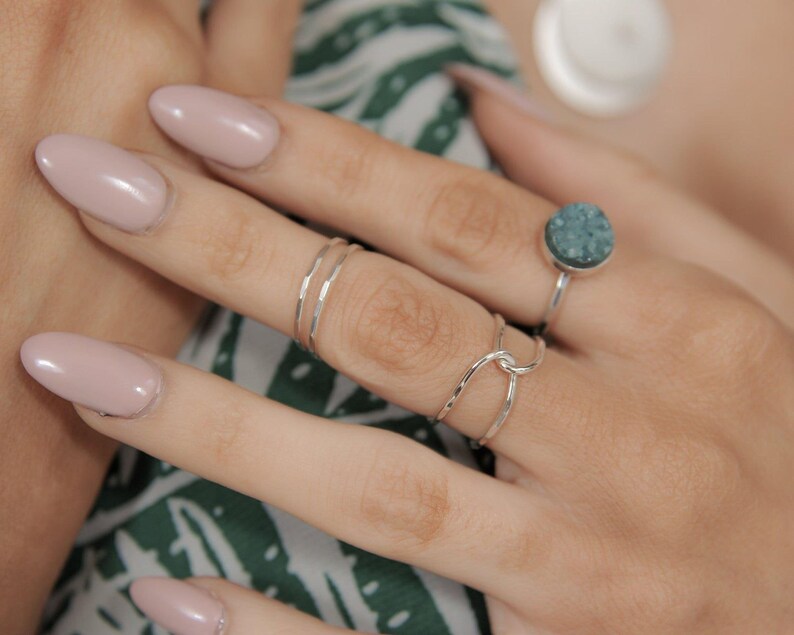 A close-up of a person's hand wearing multiple rings, including a ring with a blue stone and another ring with a twisted design.