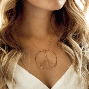 Image shows model wearing our large 14 karat yellow gold filled inner peace necklace. Our Inner Peace Sign Necklace carries a powerful message and delivers it in a chic package. An organic circular peace sign pendant sits centered on a delicate chain