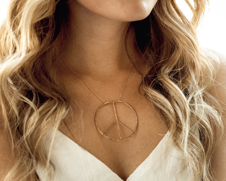 Image shows model wearing our large 14 karat yellow gold filled inner peace necklace. Our Inner Peace Sign Necklace carries a powerful message and delivers it in a chic package. An organic circular peace sign pendant sits centered on a delicate chain