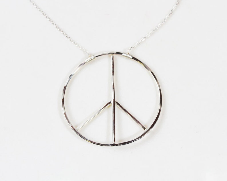 Image shows close up of our small sterling inner peace necklace. These necklaces are handcrafted and offer a lovely hand hammer texture that casts light as it is worn. Offered in sterling silver and yellow gold filled and wire wrapped to perfection.