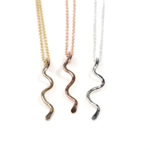 May include: Three delicate necklaces with a wavy pendant in gold, rose gold, and silver.